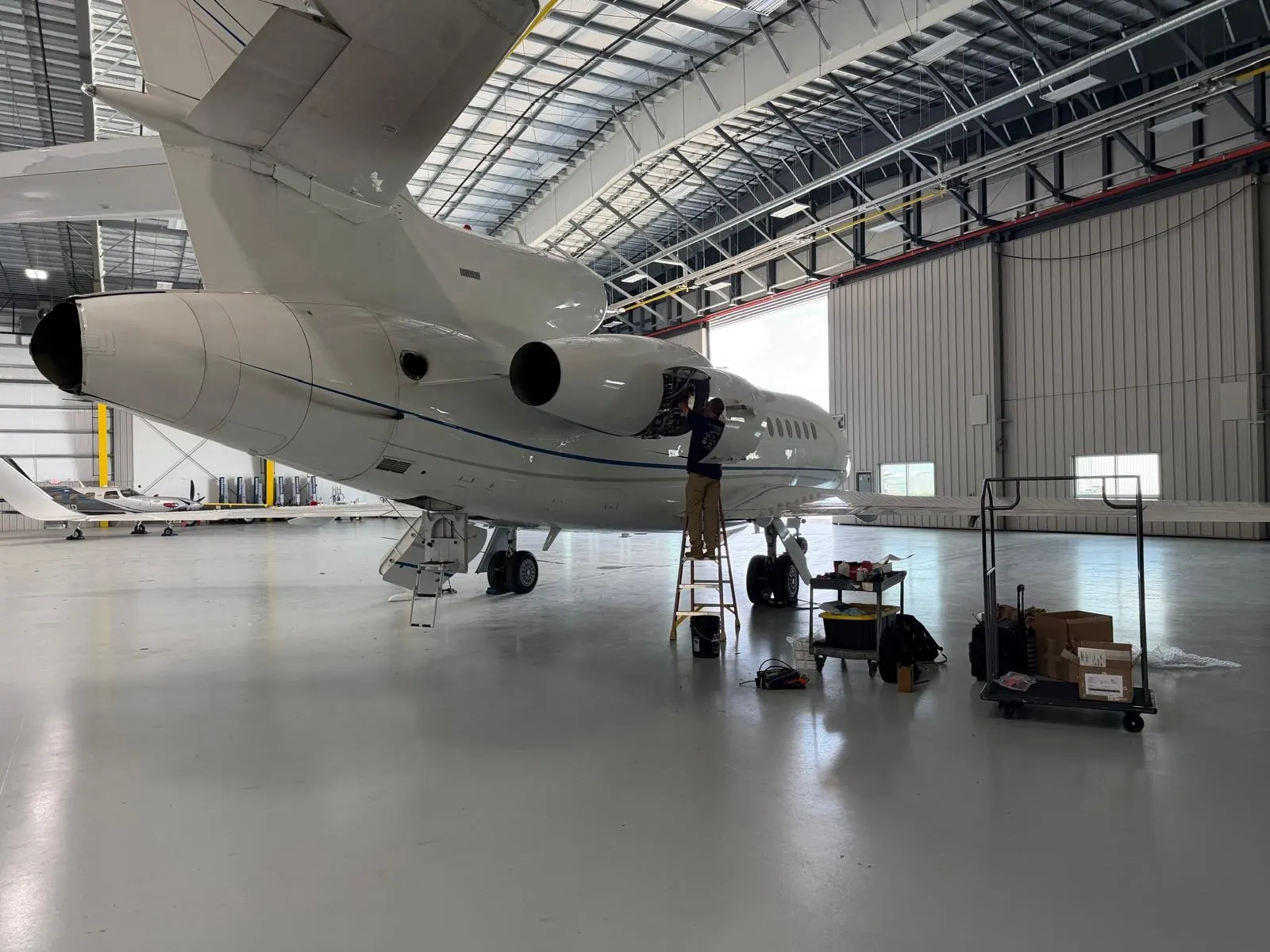 LCA technician on a ladder working in the engine area of a Dassault Falcon 900 in a hangar